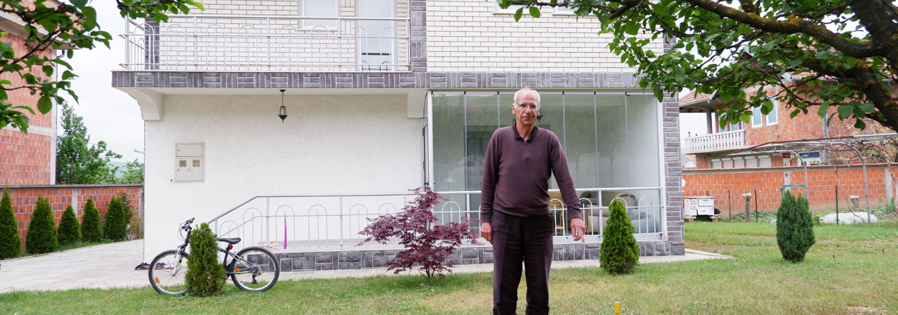Maliq stands in his garden pointing to a stick where a cluster munition was found