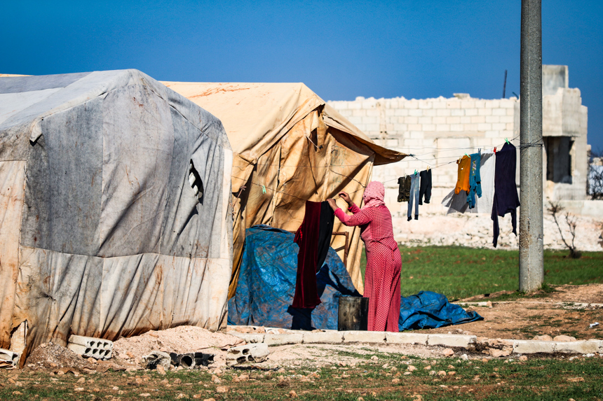 A woman stands outside a tent hanging clothes up to dry