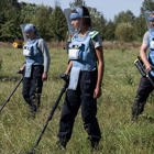 Демінери в захисному спорядженні з детекторами проводять розмінування у високій траві на фоні стіни дерев