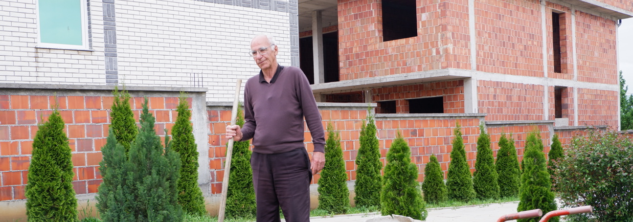 A man plants a tree outside of a house in Arllat village in Kosovo