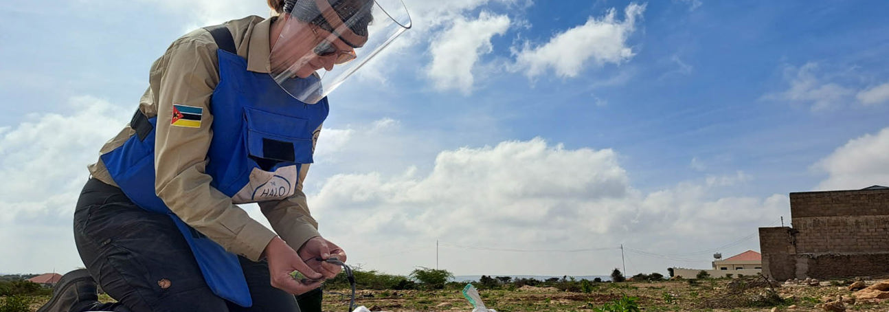 HALO staff member wearing protective gear holds a wire while kneeling on sandbags