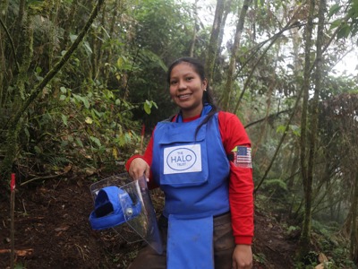 A female deminer stands in a forest with her PPE