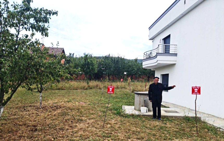 Jakup Bujupi stands in front of his house with mine warning signs in front