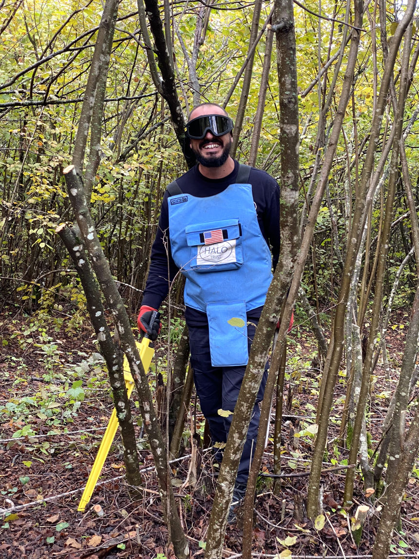 Kaltrim Hoxha, Assistant Team Leader, smiles in a forest with a Schonstedt Magnetic Locator in hand