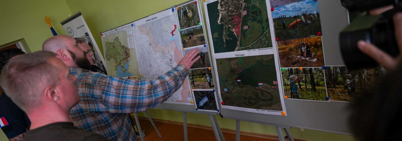 Men look at pinned maps and pictures of demining activities in the Kharkiv region