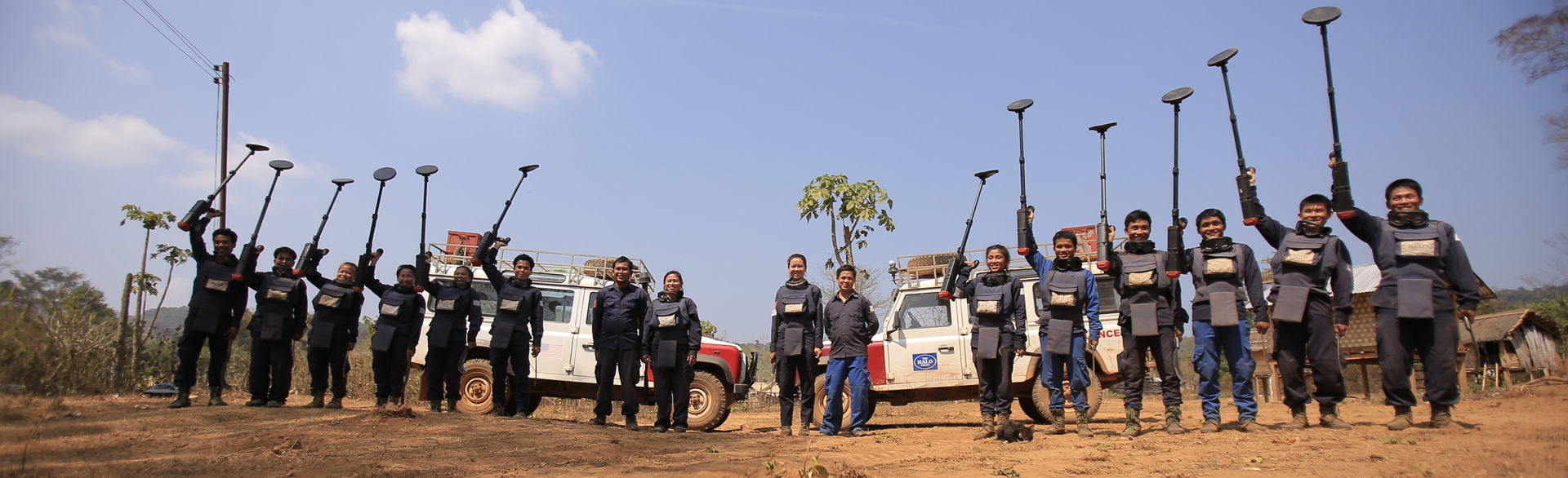 A group of HALO's deminers in Laos smiling and holding up their metal detectors