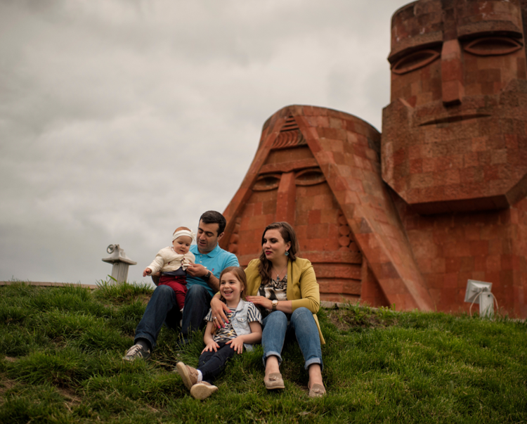 A family sit on a hill in front of a large stone face carving