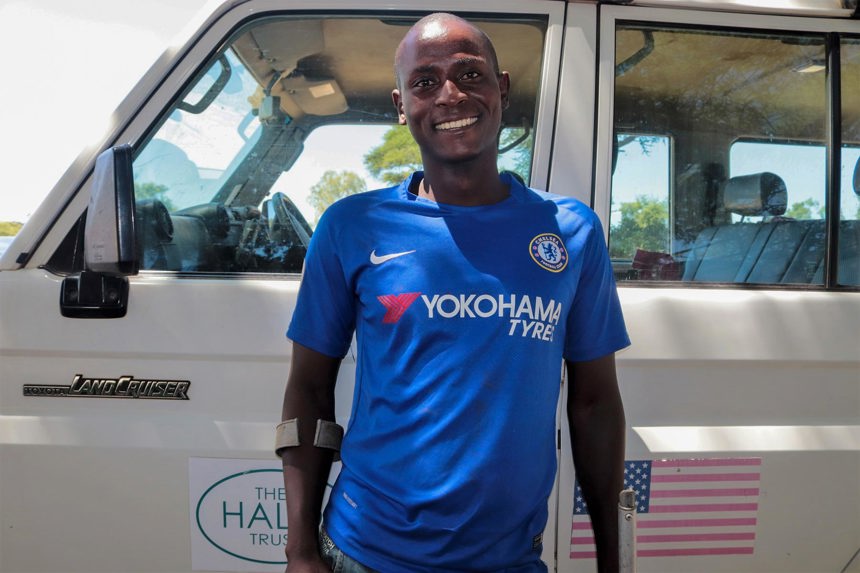 Daniel Kutsakatika, a landmine survivor smiles in front of a HALO van