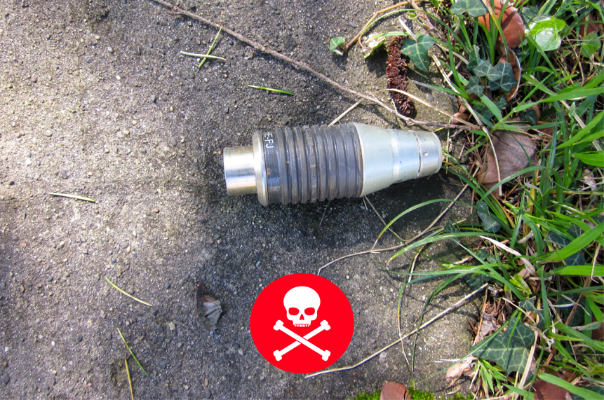 An unexploded ordinance lays on the concrete with a deadly warning logo in the picture
