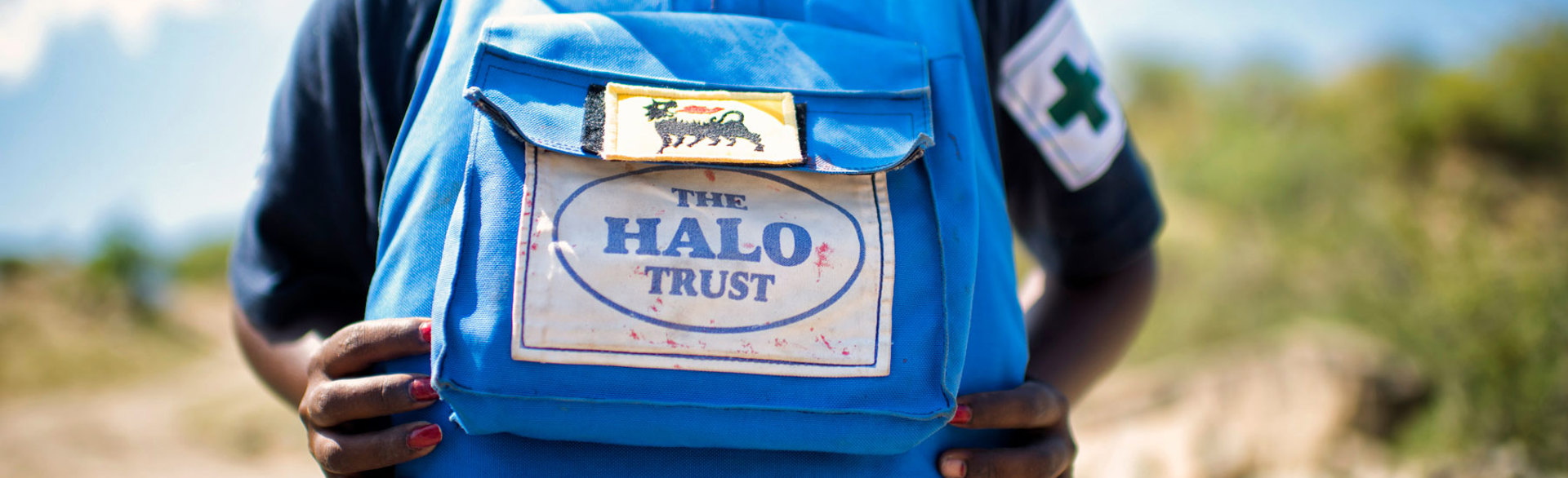 A woman wearing HALO Trust personal protective equipment displays the HALO logo