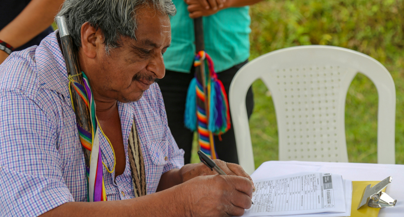 A man sits down to write on a paper form outside