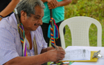 A man sits down to write on a paper form outside