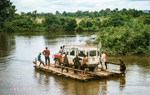 A large vehicle and group of people cross a river on rustic wooden boat in Cambodia