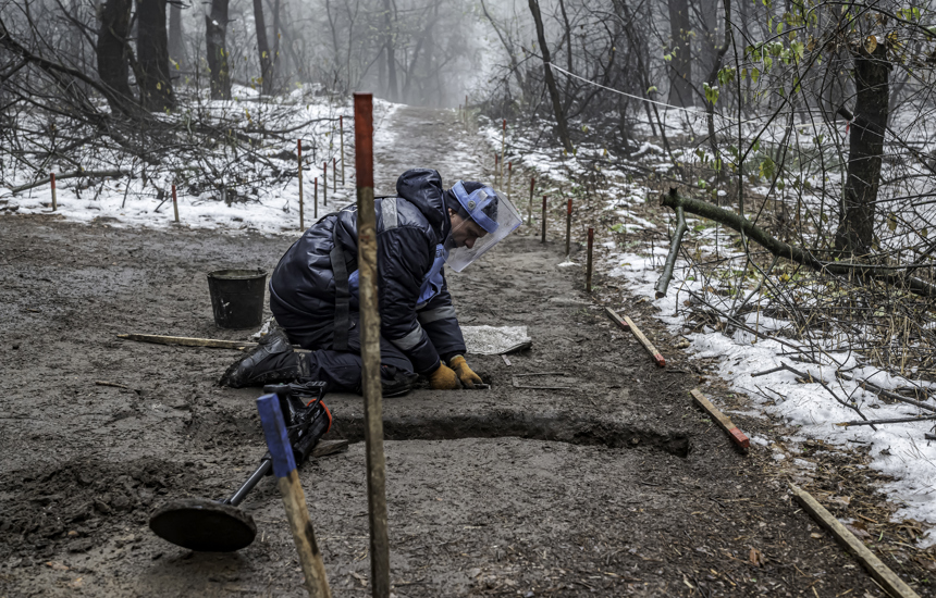 A deminer excavates the soil whiles wearing PPE in a snowy mine marked area