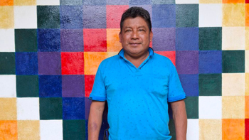 A middle-aged man wearing a blue polo stands in front of a colorful geometric mural.
