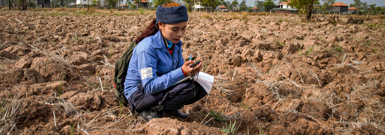 HALO staff member learning how to use a GPS in a field in Cambodia