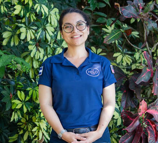 Lisseth wears a HALO polo shirt, standing in front of green and pink plants