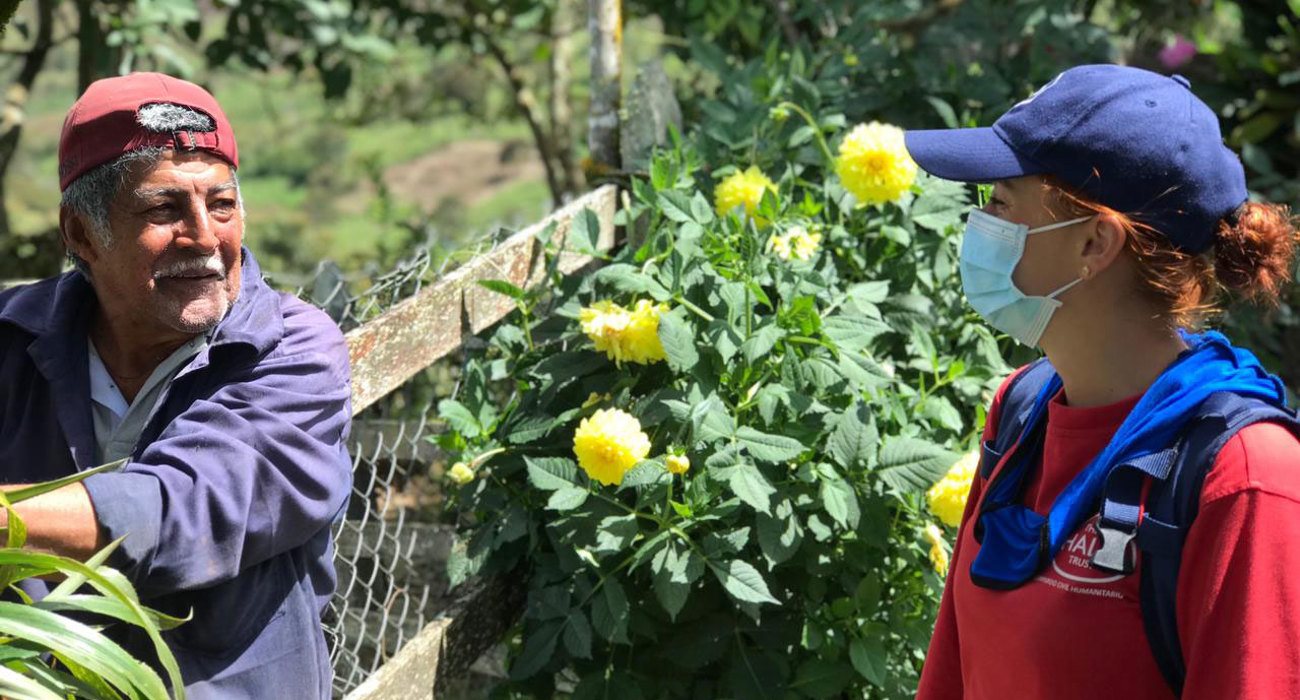 A man tends to plants outside whilst talking with a HALO staff member