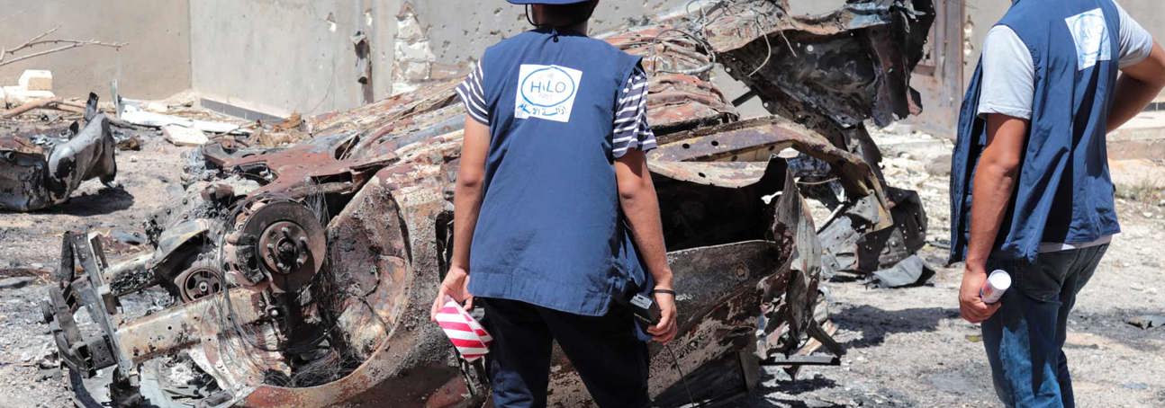 HALO staff members stand in front of a destroyed vehicle in Tripoli