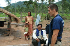 A woman and a child stand together outside a straw shelter with two deminers 
