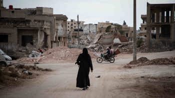 Woman dressed in black, walking through a street in Syria surrounded by rubble from destroyed buildings