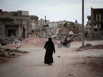 Woman dressed in black, walking through a street in Syria surrounded by rubble from destroyed buildings