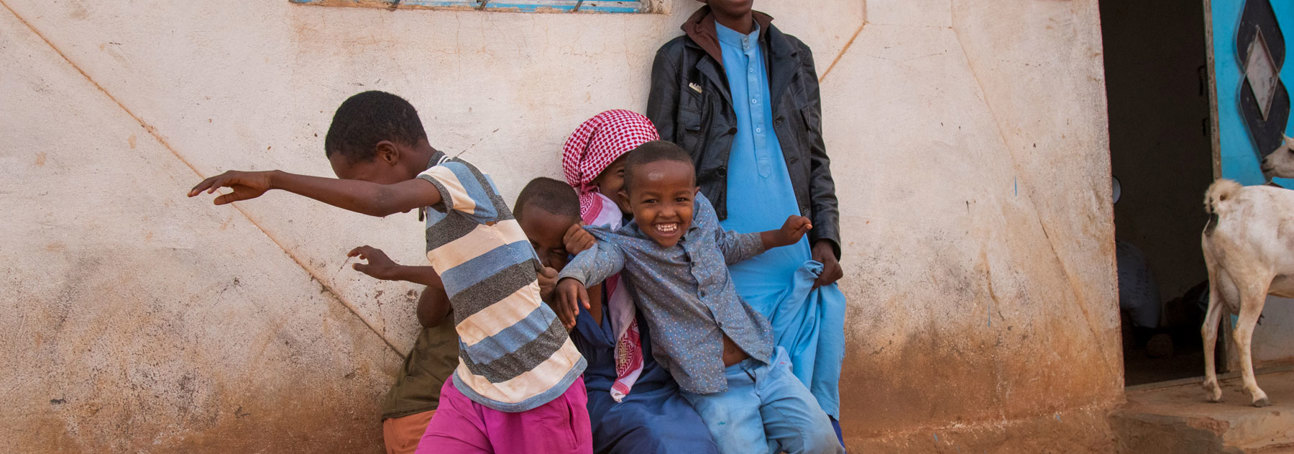 A group of children play outside a building next to an adult and goat in Somaliland 