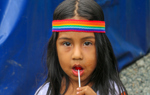 A child wears a rainbow bandana whilst eating a lolly pop