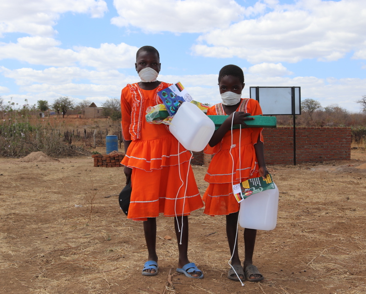 Two Zambian children in a rural area holding bottles and Covid-19 leaflets