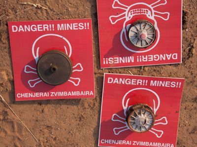 Mine warning signs lay on the soil with mines on top of them