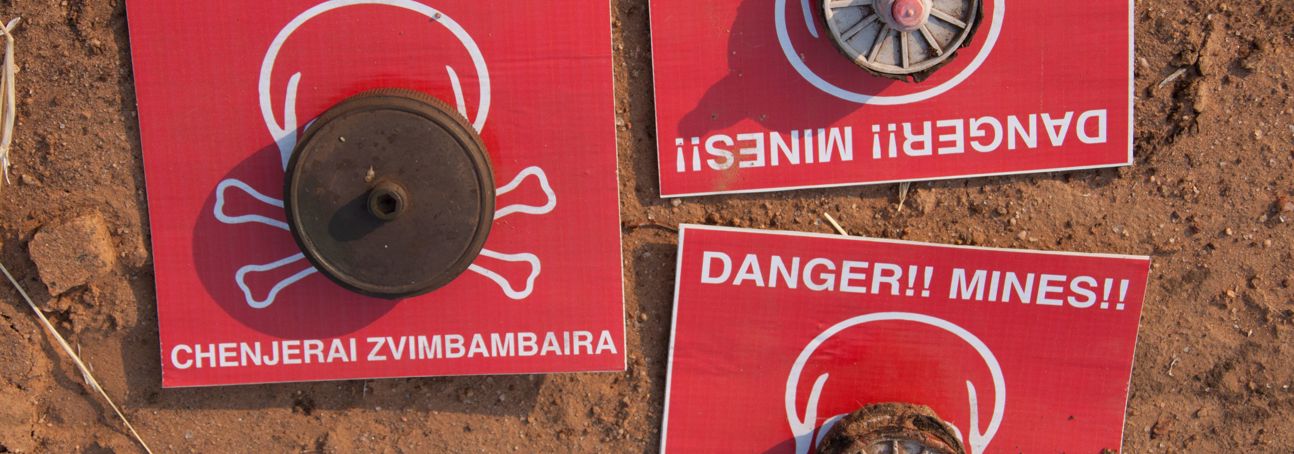 Mine warning signs lay on the soil with mines on top of them