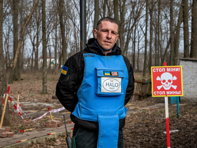 A deminer poses next to a mine warning sign in the forest