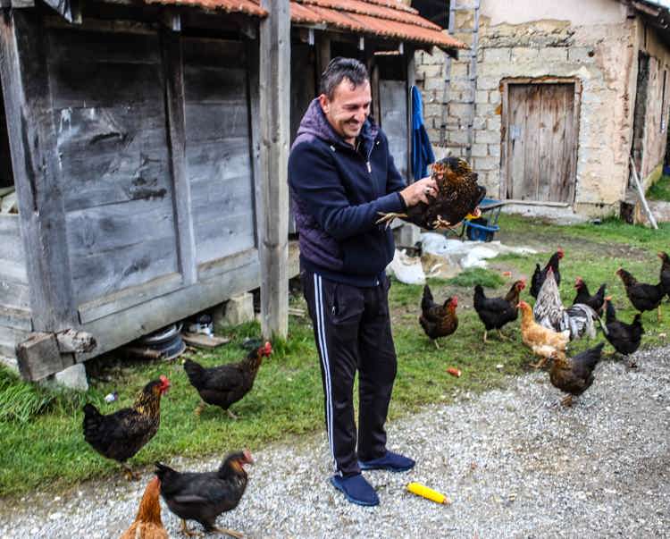 In Arllat village a man holds a chicken as other chickens surround him