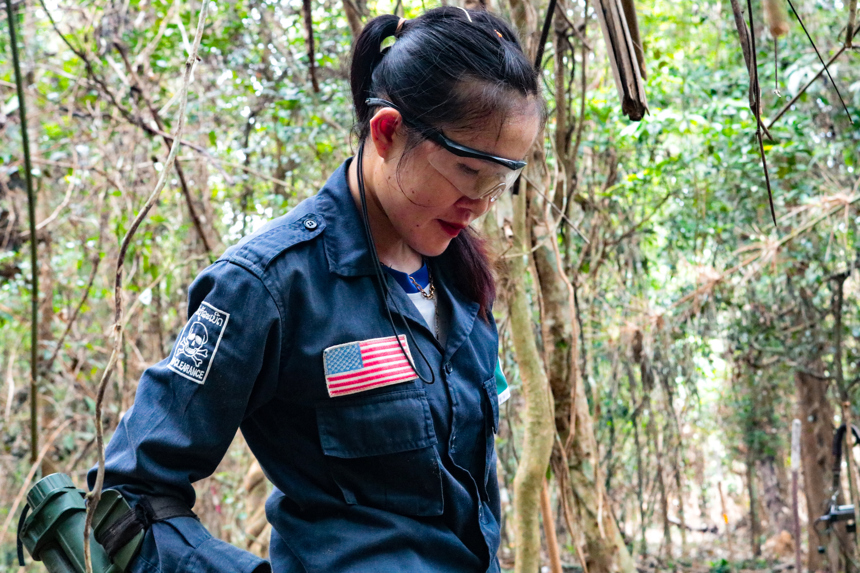HALO technician, Kong Keo, stands in a forest wearing protective glasses