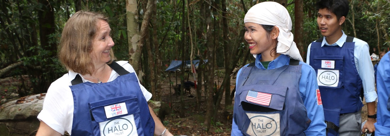 Two HALO staff smile together wearing uniforms with a UK aid badge and American flag