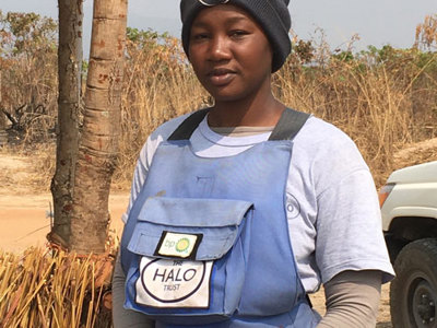 A woman wearing PPE stands in a rural area wearing HALO's PPE with a bp badge on the front