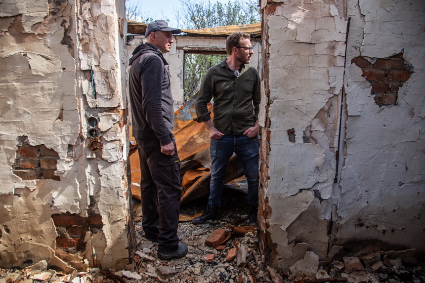 Two men stand inside the remains of a home that has been destroyed