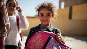 Syrian girl holding a backpack and smiling