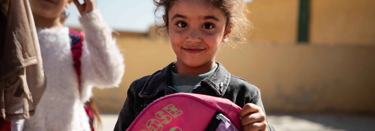 Syrian girl holding a backpack and smiling