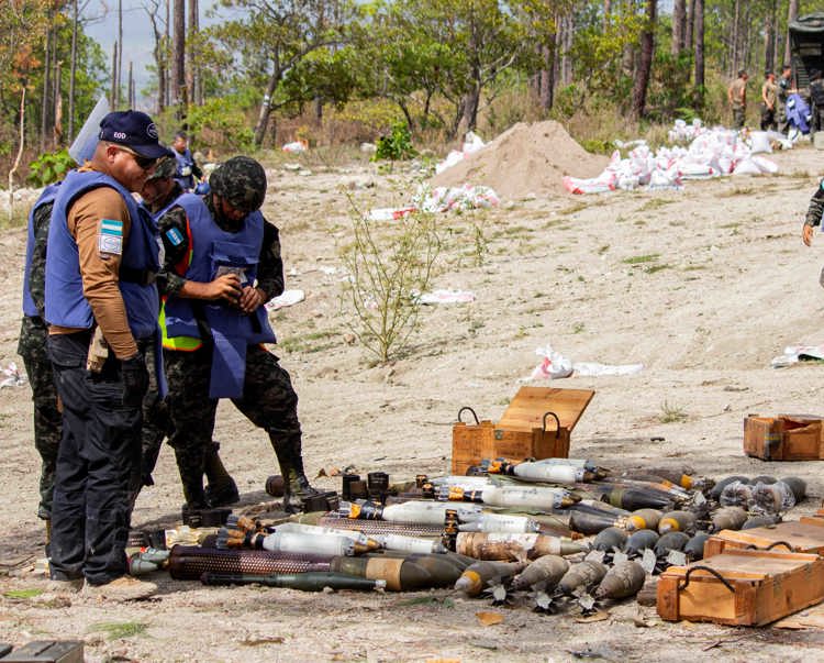 People in HALO vests gather round a stockpile of weapons in Honduras