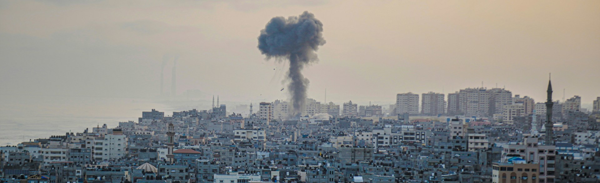 An aerial view of the damaged city of Gaza with a plume of smoke from an explosion rising in the distance