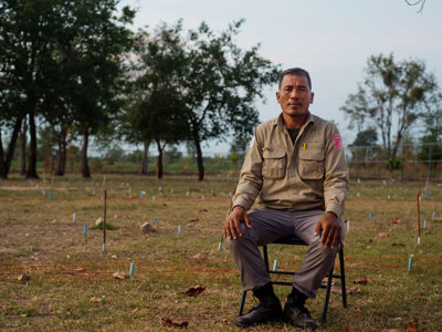 Un Ek, the Head of training in Cambodia, sits in a marked minefield