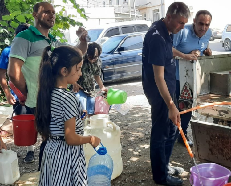 Children and adults stand around an outdoor tap to fill up containers with water