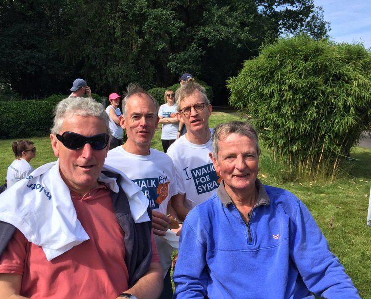 Four men smile and pose on grass with their "walk for Syria" T-shirts