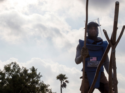 A HALO deminer in Sri Lanka stands in PPE displaying the US flag while wearing a visor