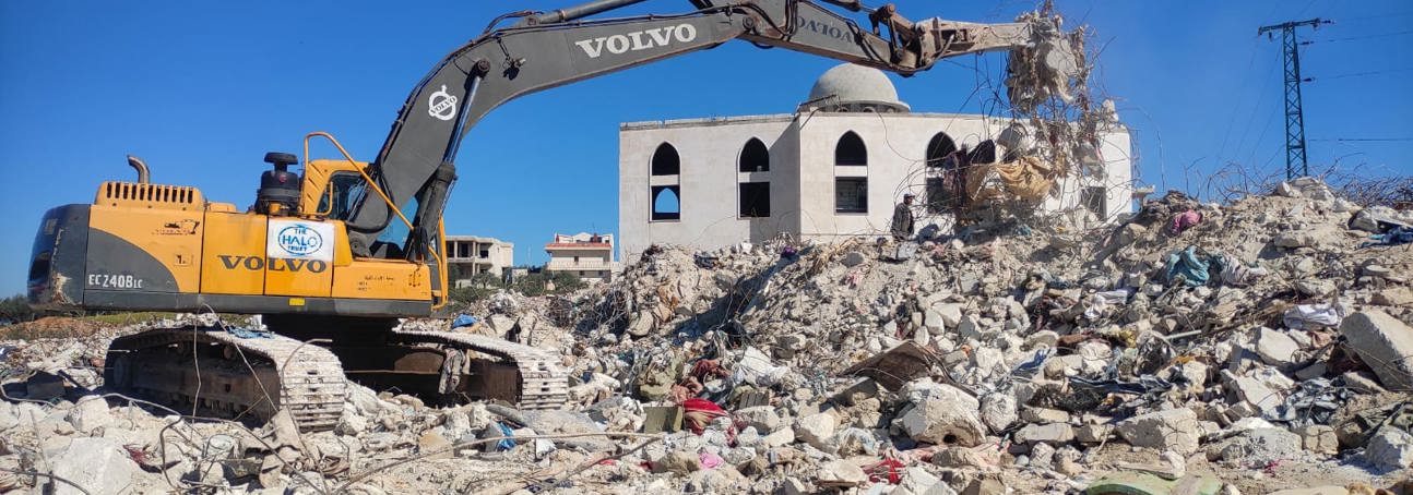 Excavator picks up debris from a large pile of rubble outside