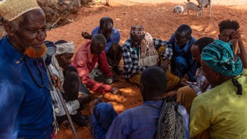Group of Somaliland men sitting on the orange tinted soil play a game with date stones