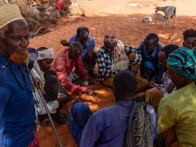 Group of Somaliland men sitting on the orange tinted soil play a game with date stones