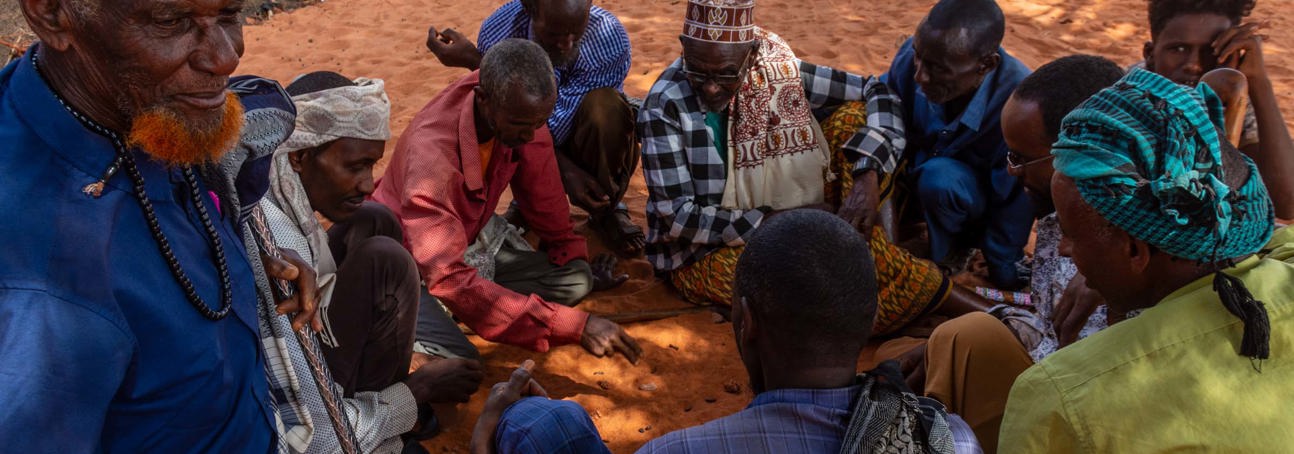 Group of Somaliland men sitting on the orange tinted soil play a game with date stones