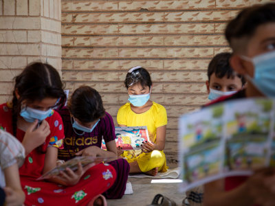 Children sit down with leaflets in an explosive ordnance risk education session